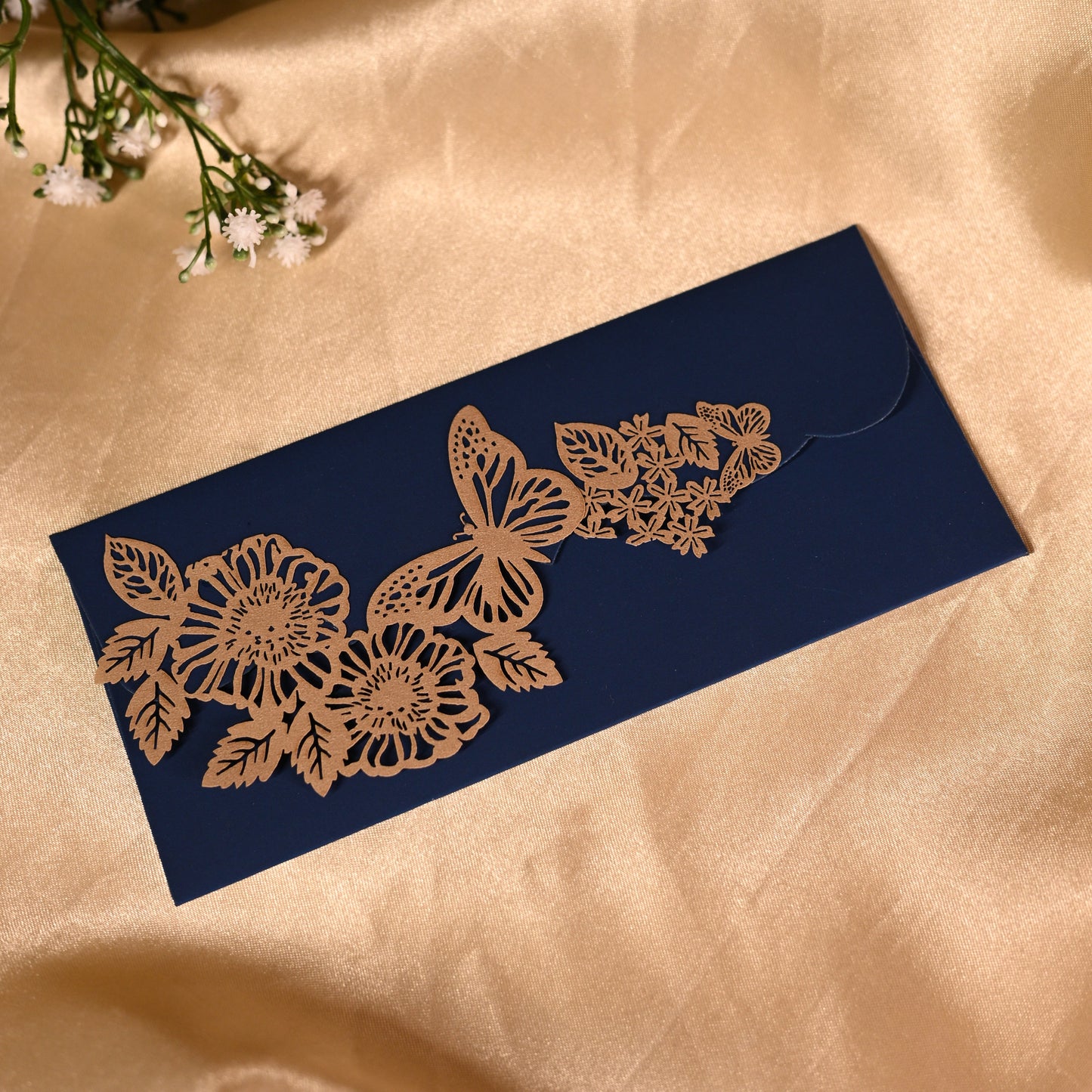Navy blue envelope with gold floral and butterfly designs on a beige fabric background