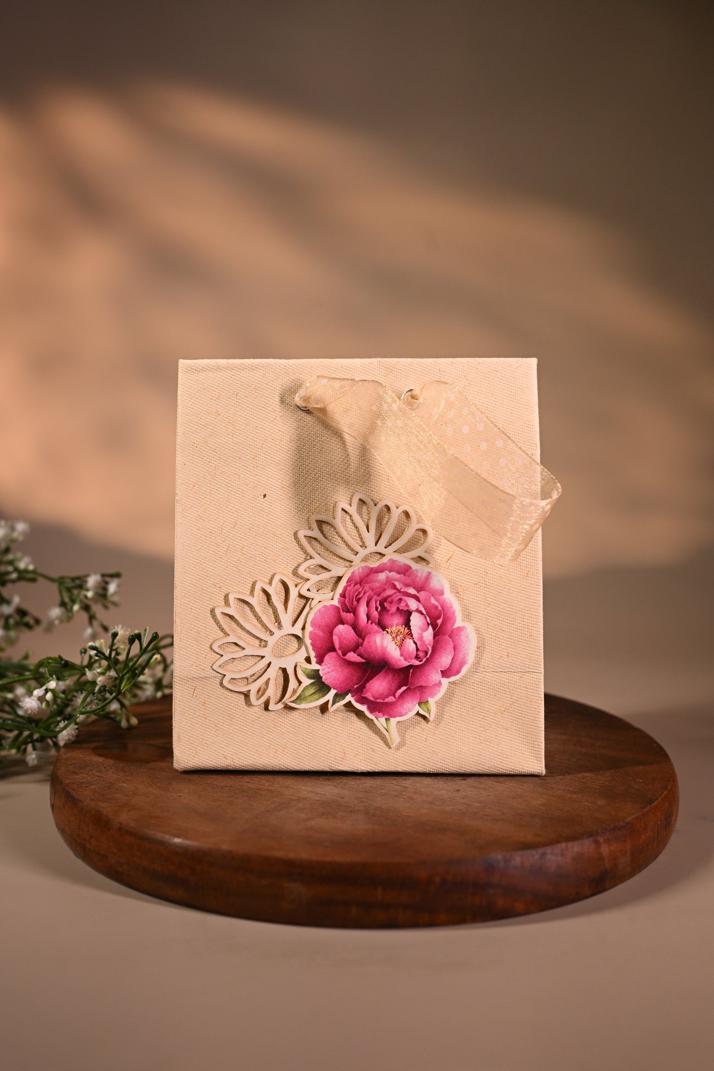 This is a pretty gift bag made from strong paper. It has a beautiful golden floral design with pink flower sticker on the front. The bag has gold ribbon handles, making it easy to carry and giving it a stylish touch.