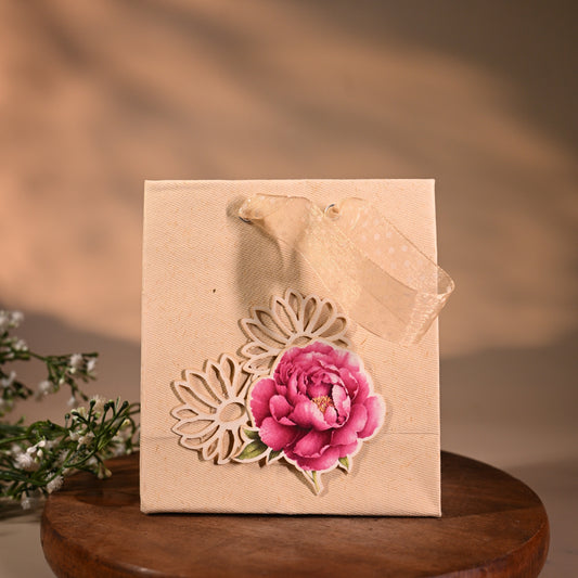 This is a pretty gift bag made from strong paper. It has a beautiful golden floral design with pink flower sticker on the front. The bag has gold ribbon handles, making it easy to carry and giving it a stylish touch.