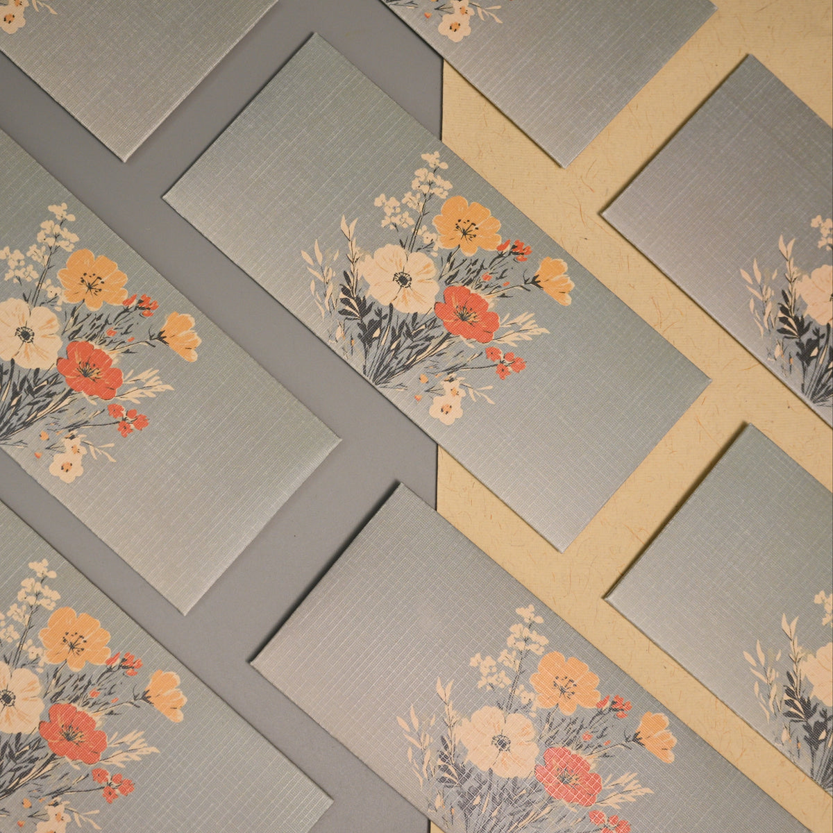 Envelopes arranged diagonally on a gray surface, each printed with a floral bouquet design in orange, cream, and yellow tones.