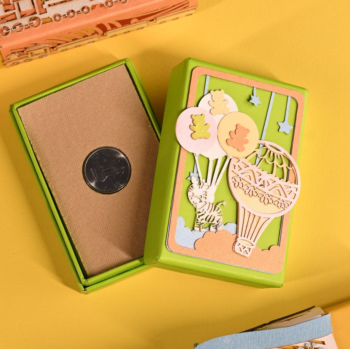 Three colorful illustrated gift boxes arranged on a solid yellow background. One box is open, showing a brown textured insert with a round black button or snap in the center.