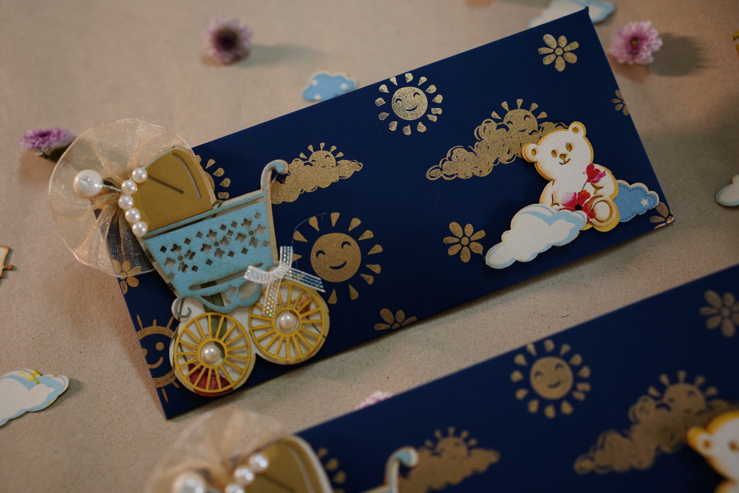 A blue envelope with a decorative baby pram and teddy bear design, with sun and clouds in the background