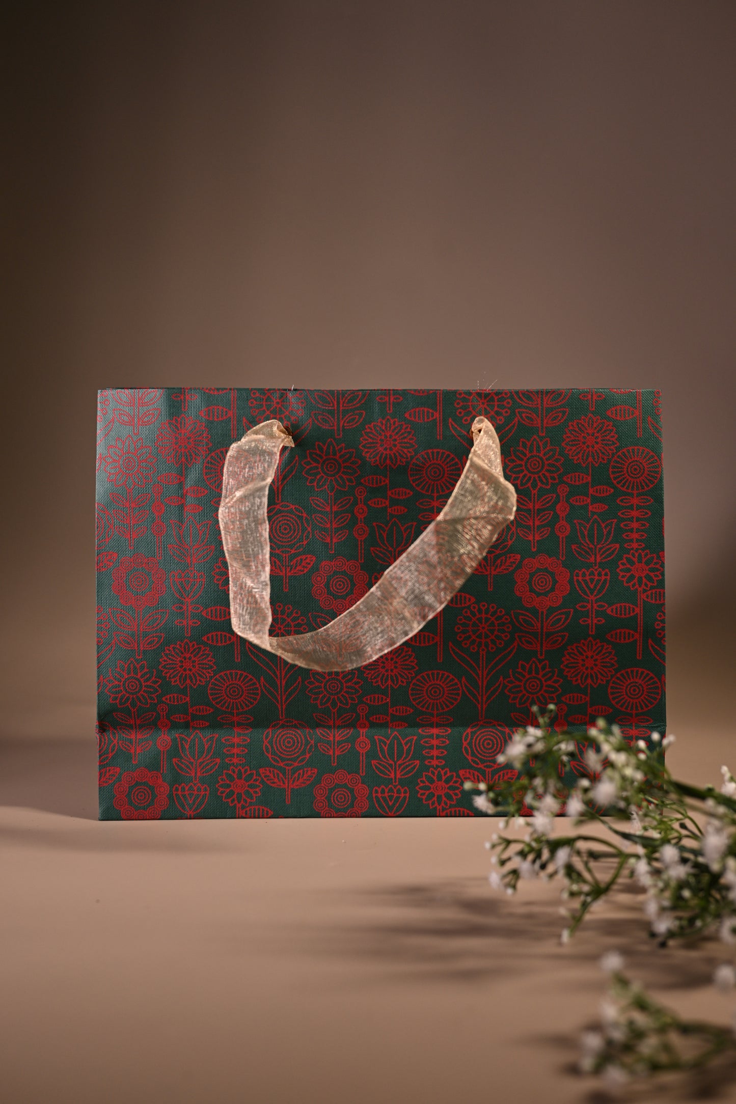 green paper bag with red floral motifs and ribbon handle