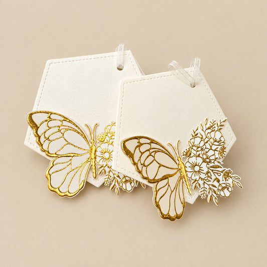 A set of white gift tags with gold foil-embossed butterfly designs, tied with a ribbon.