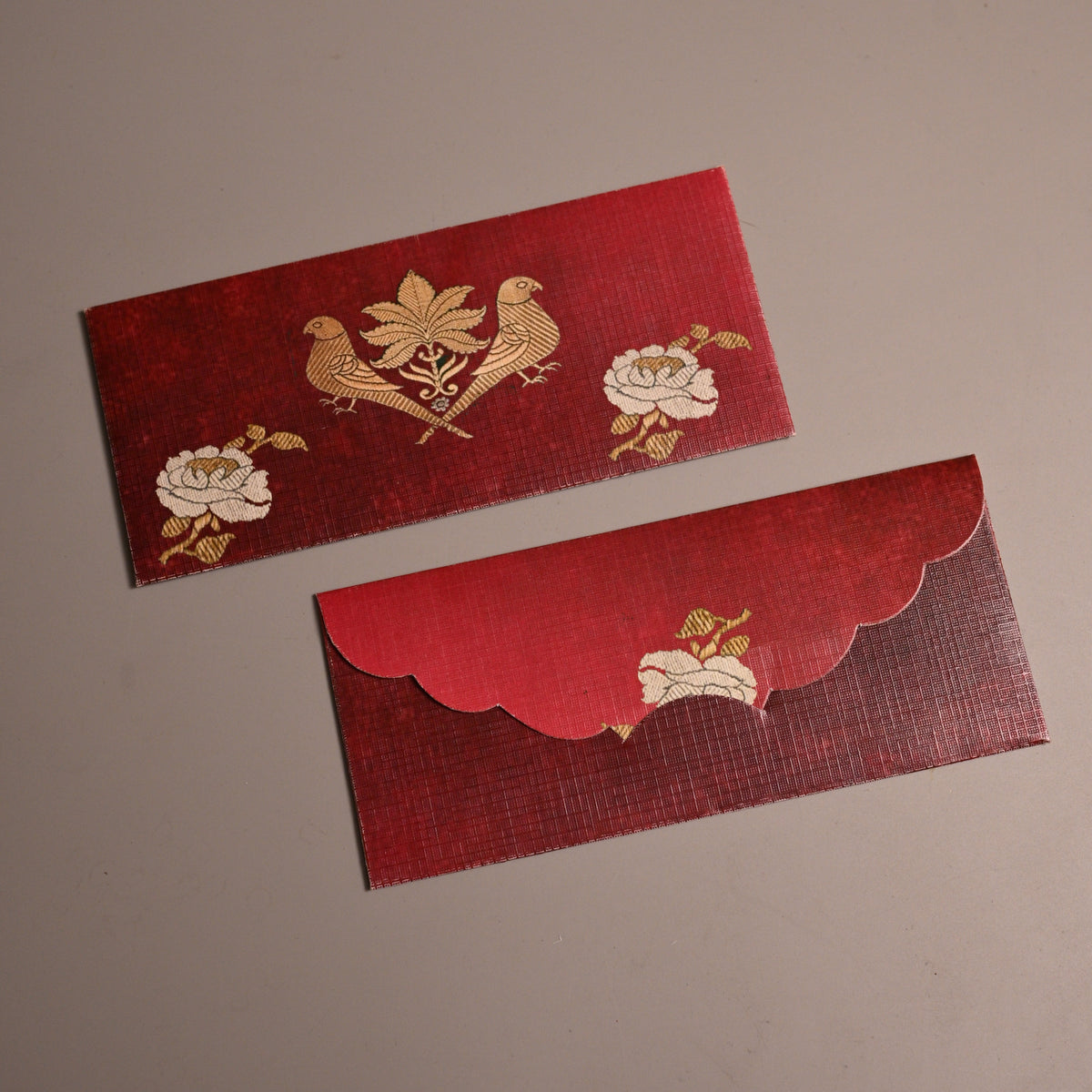Two red Chinese New Year envelopes with gold foil bird and floral designs, displayed on a neutral gray background.