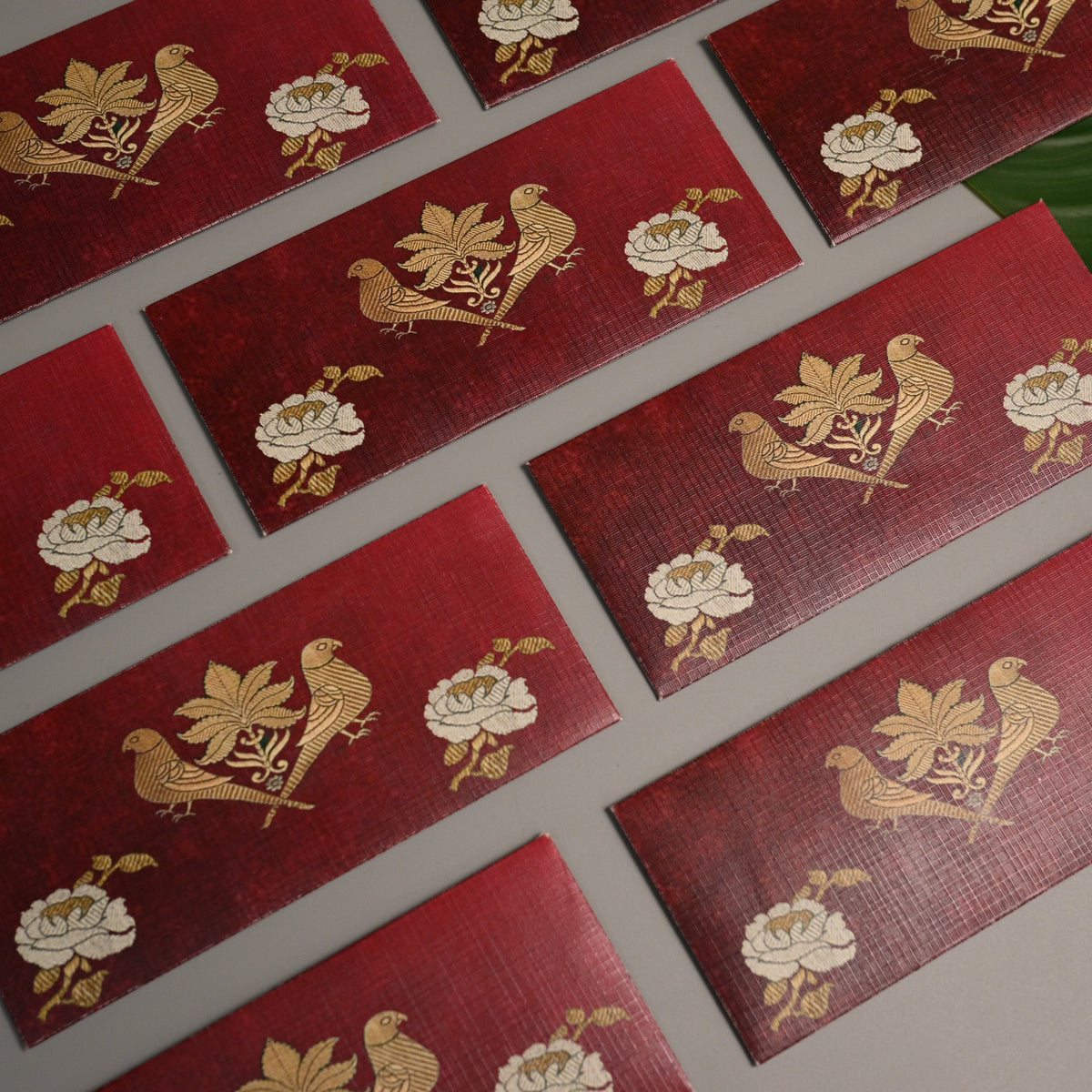 A set of rectangular red envelopes with textured gold foil designs featuring birds, lotus flowers, and leaves