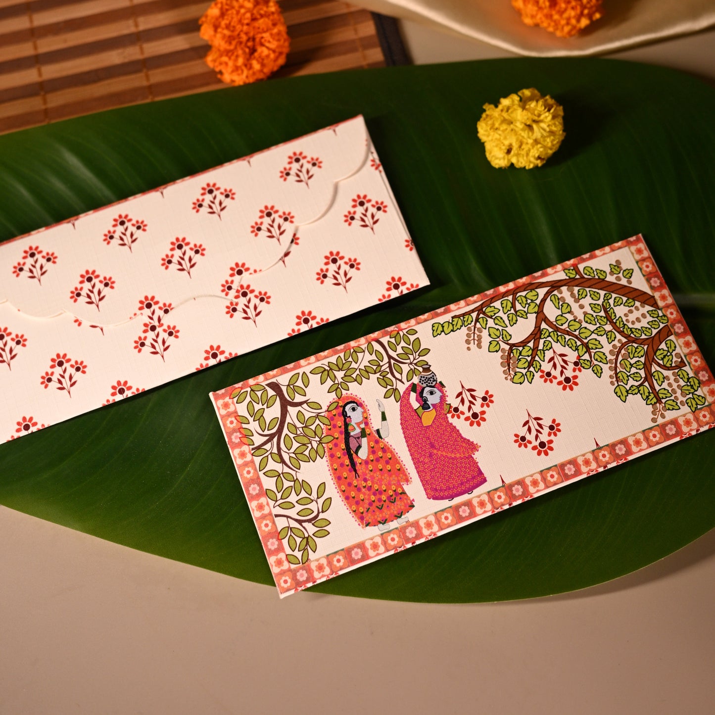 Decorative envelopes with floral designs on a green leaf, with a beige fabric and small flowers in the background