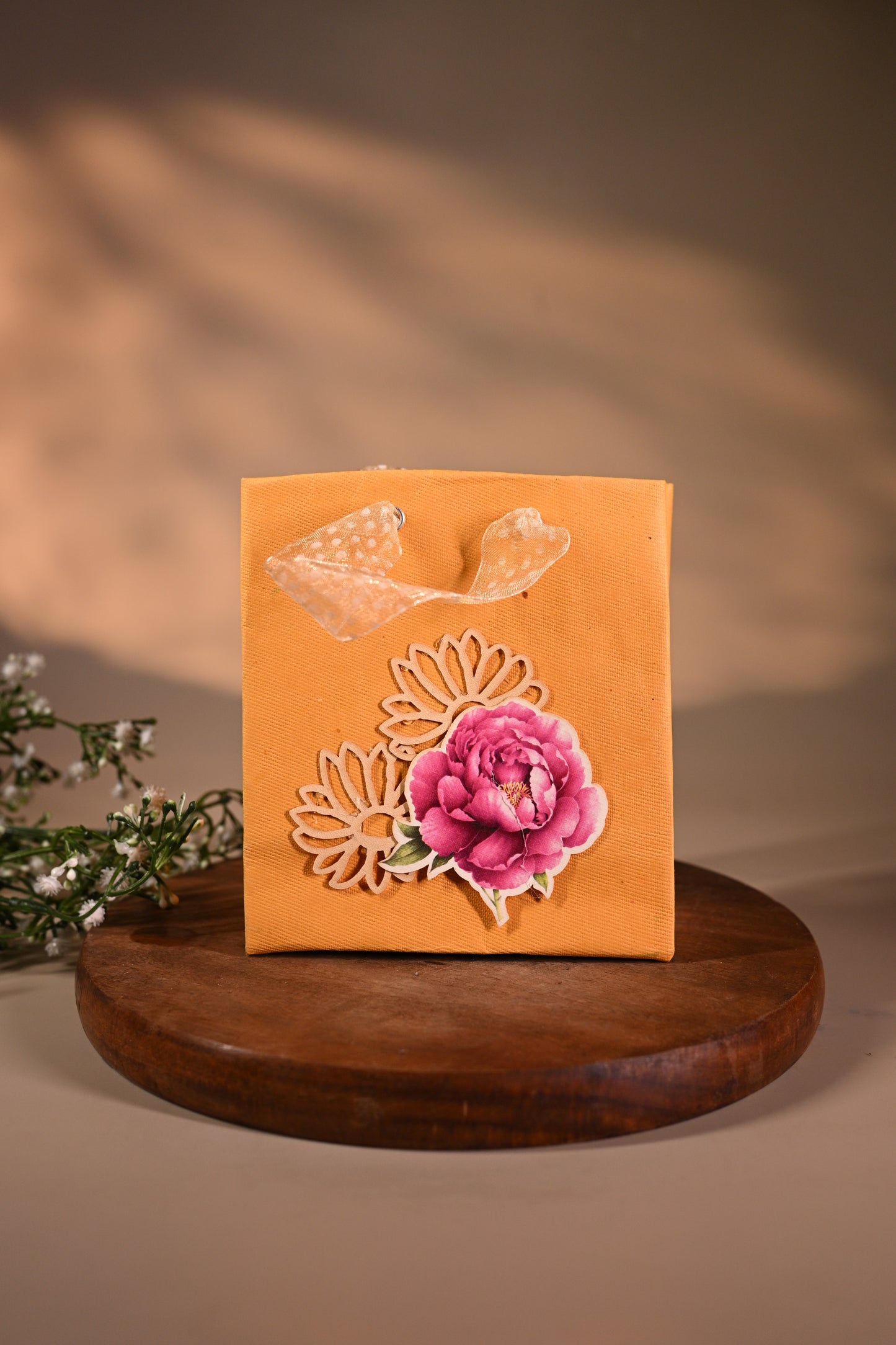 This is a pretty gift bag made from strong paper. It has a beautiful golden floral design with pink flower sticker on the front. The bag has gold ribbon handles, making it easy to carry and giving it a stylish touch.