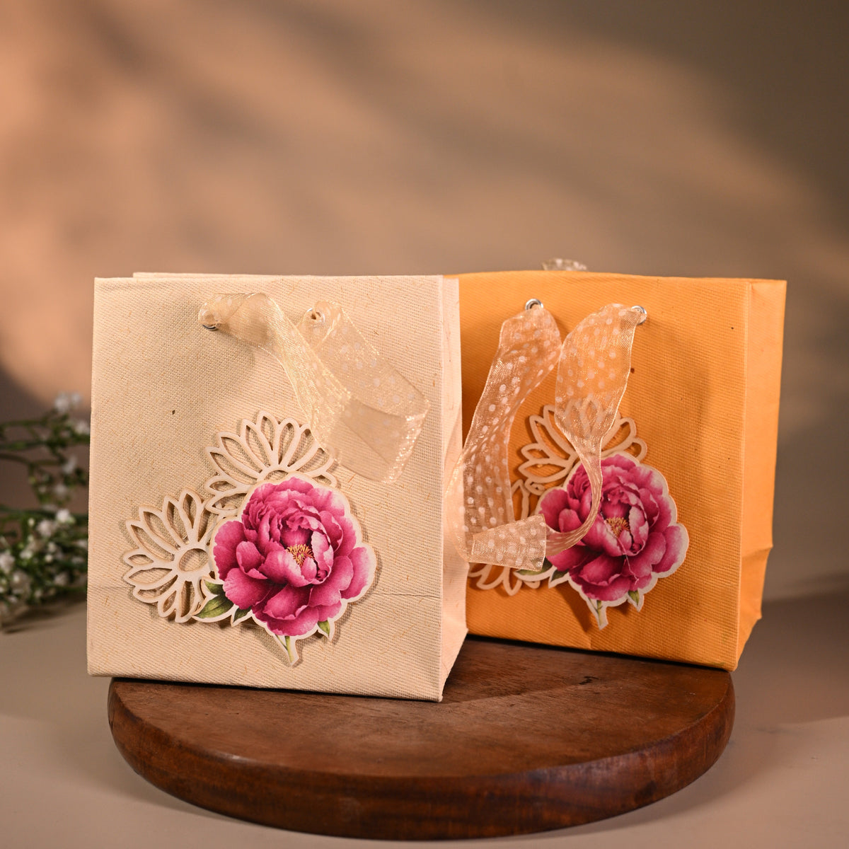 This is a pretty gift bag made from strong paper. It has a beautiful golden floral design with pink flower sticker on the front. The bag has gold ribbon handles, making it easy to carry and giving it a stylish touch.
