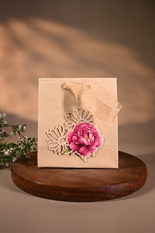 This is a pretty gift bag made from strong paper. It has a beautiful golden floral design with pink flower sticker on the front. The bag has gold ribbon handles, making it easy to carry and giving it a stylish touch.