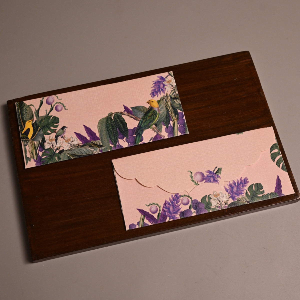 A rectangular dark brown wooden board with two decorative floral paper inserts, photographed on a plain taupe background.