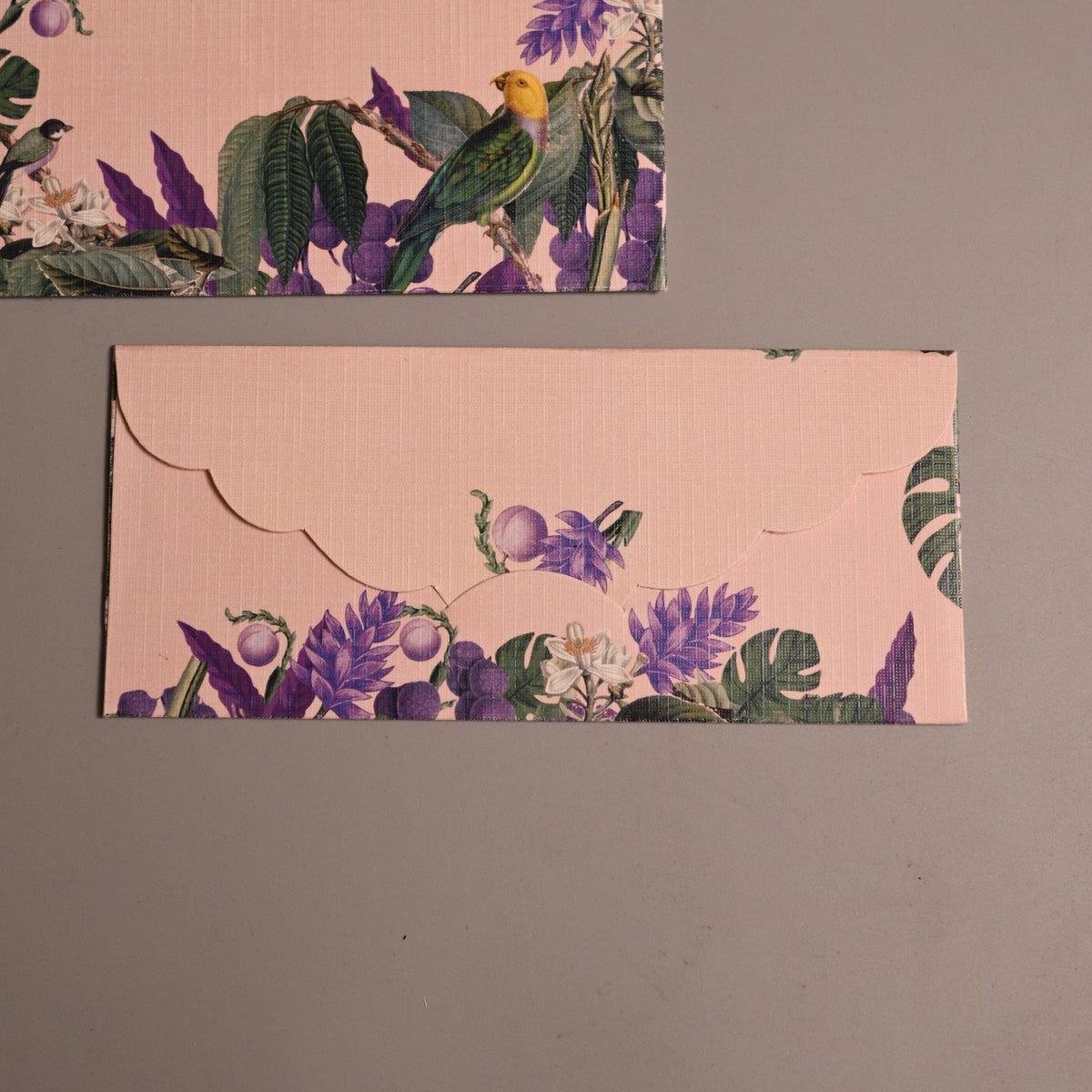 Two rectangular envelopes with a light pink background and a tropical floral and bird print