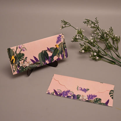 A pink floral clutch purse and matching flat card or envelope set with purple flowers, green leaves, and butterfly motifs, styled on a neutral gray background with small white flowers.
