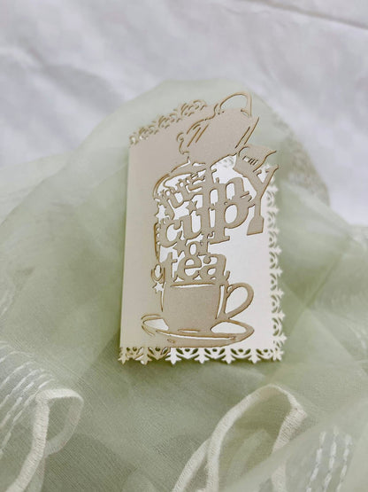 Decorative white gift tags with laser-cutwork, featuring a teapot, teacup and saucer, writing