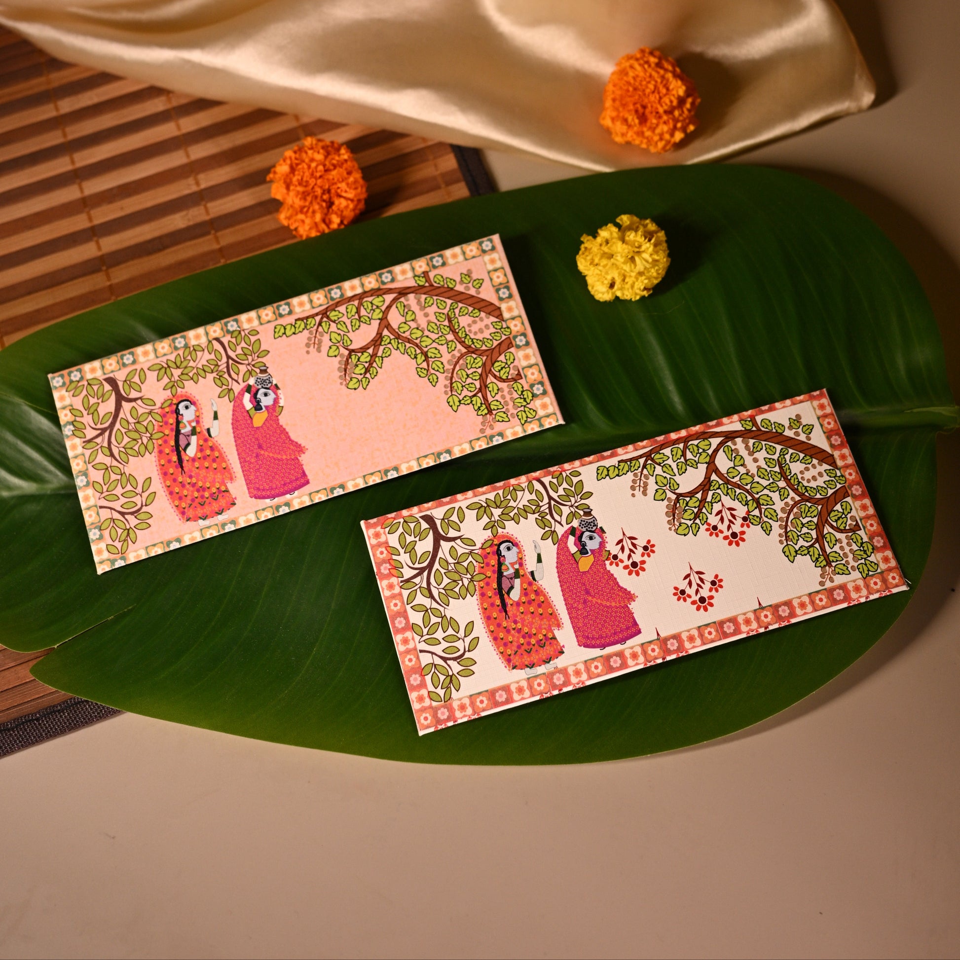Decorative envelopes with floral designs on a green leaf, with a beige fabric and small flowers in the background