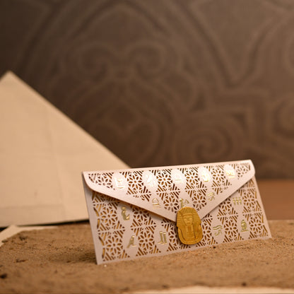 A white envelope-style card or small pouch with an intricate laser-cut geometric pattern and a gold seal.