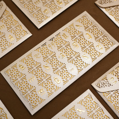 White paper invitation cards and matching envelopes with intricate laser-cut geometric patterns and gold foil lettering, arranged diagonally on a dark brown background.