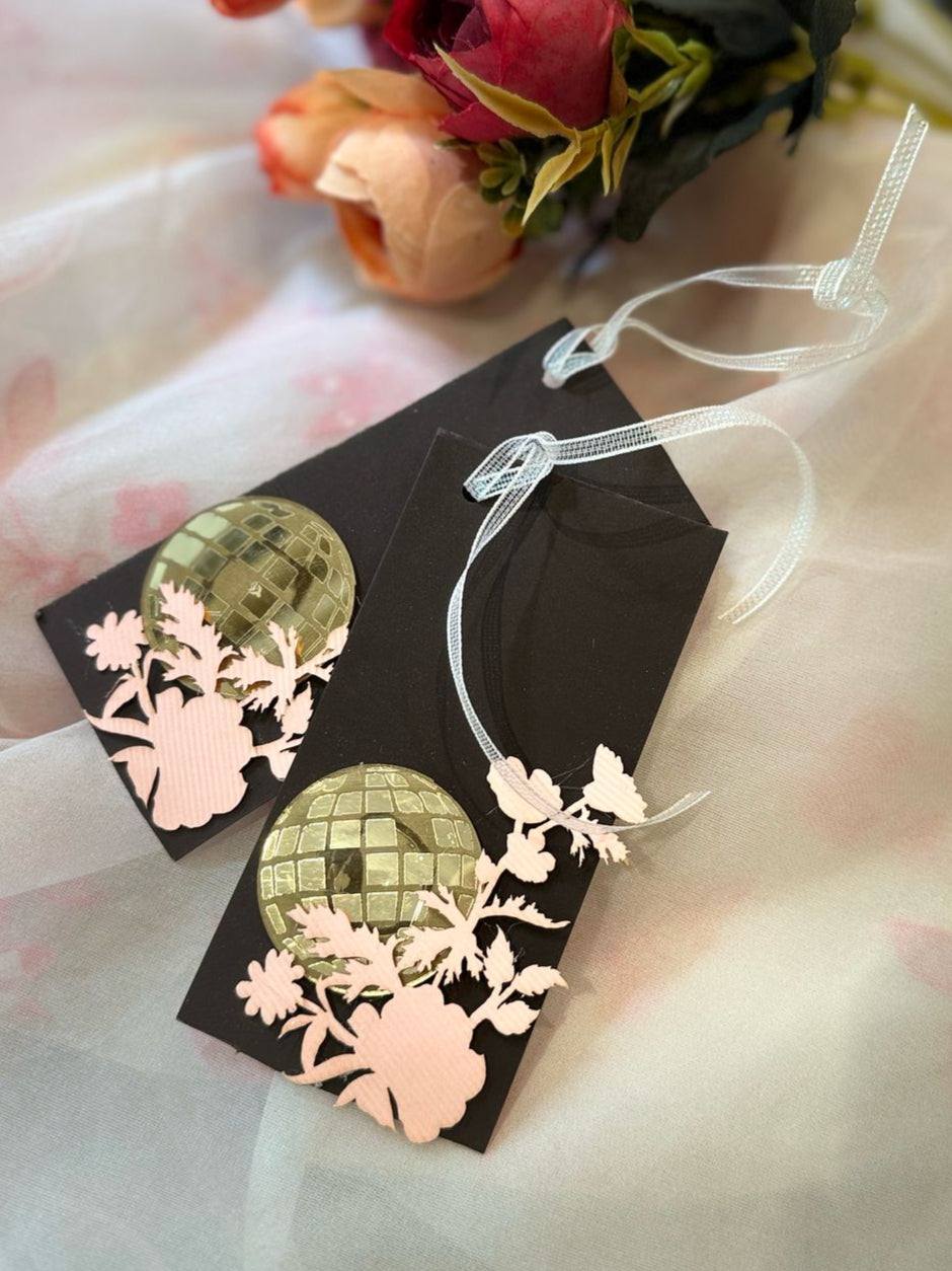 A set of brown gift tags with a reflective acrylic disco ball design and blush pink laser-cut floral silhouettes, attached with a white string to a ribbon.