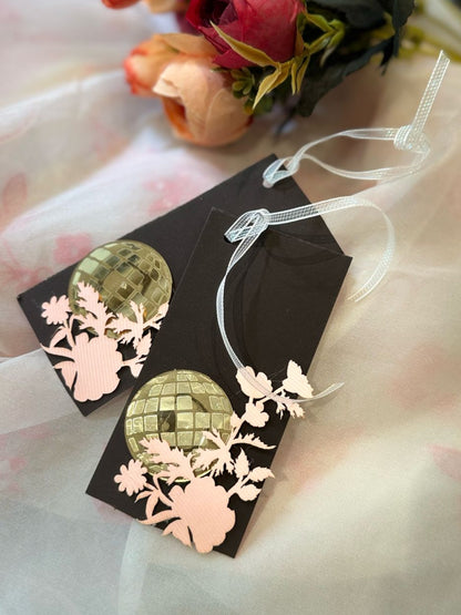 A set of brown gift tags with a reflective acrylic disco ball design and blush pink laser-cut floral silhouettes, attached with a white string to a ribbon.
