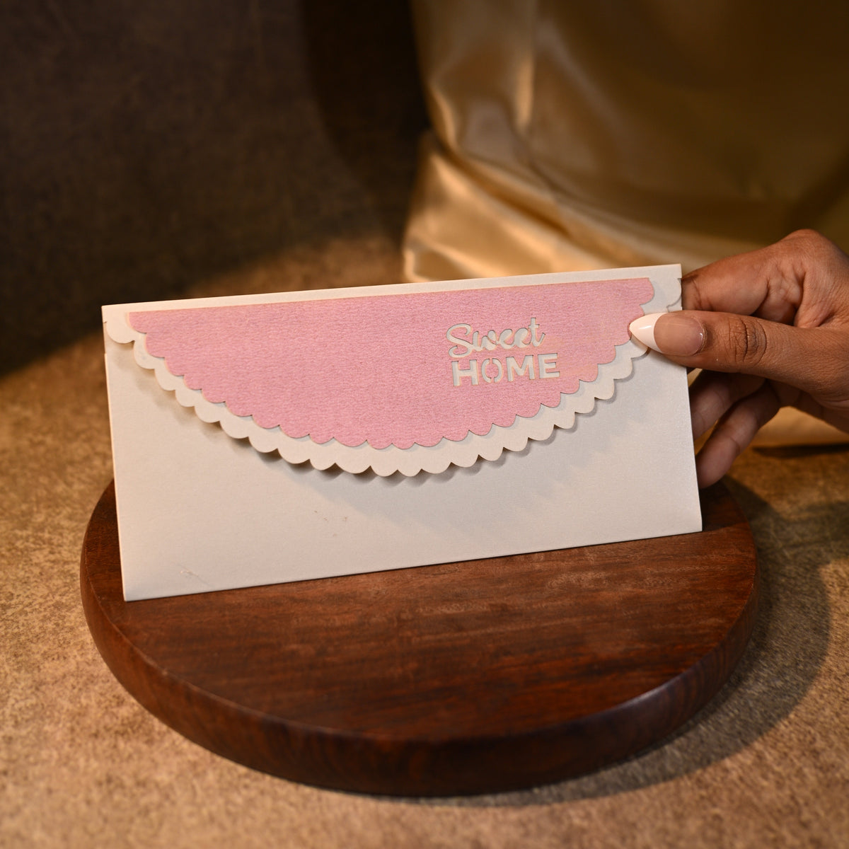 Hand holding a pink and white card with 'Sweet Home' text against a blurred background