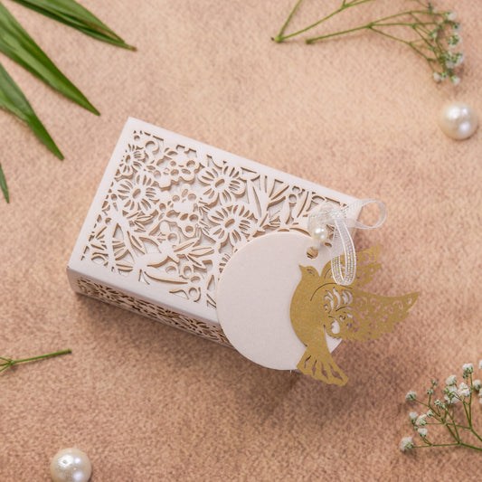 A small white decorative gift box with laser-cut floral patterns and a gold bird silhouette charm.