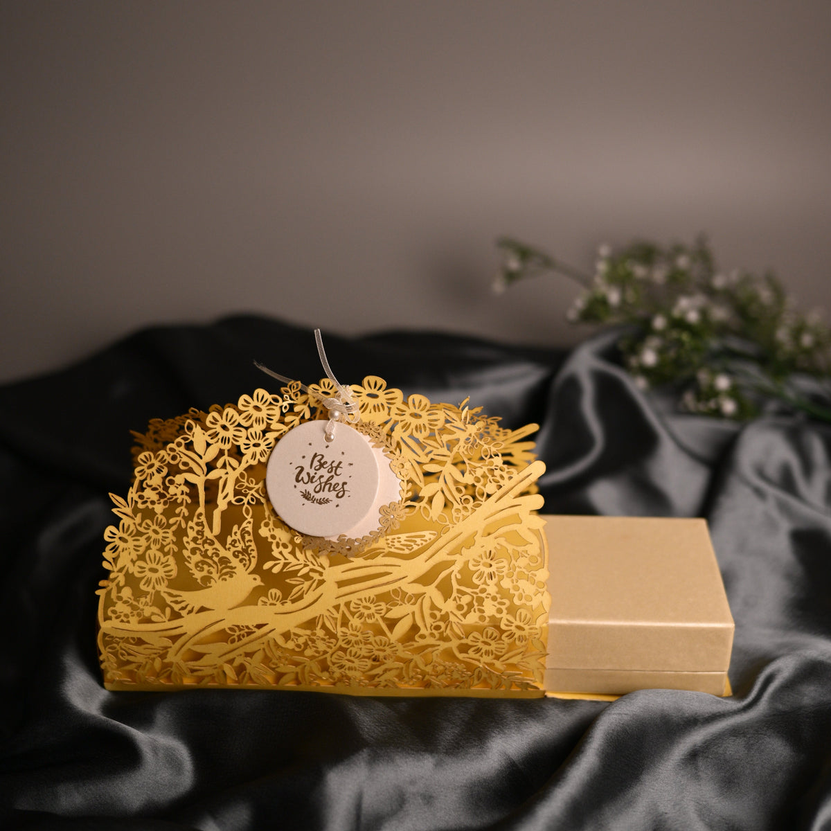 A gold laser-cut decorative box with a circular white tag reading 'Best Wishes'
