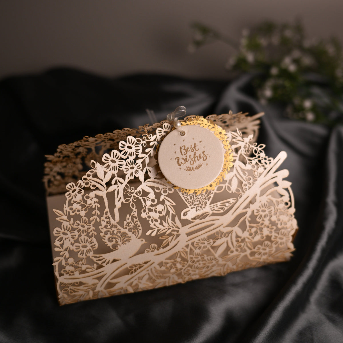A laser-cut kraft paper envelope with intricate floral and bird designs, featuring a round hanging tag that reads 'The Best wishes'