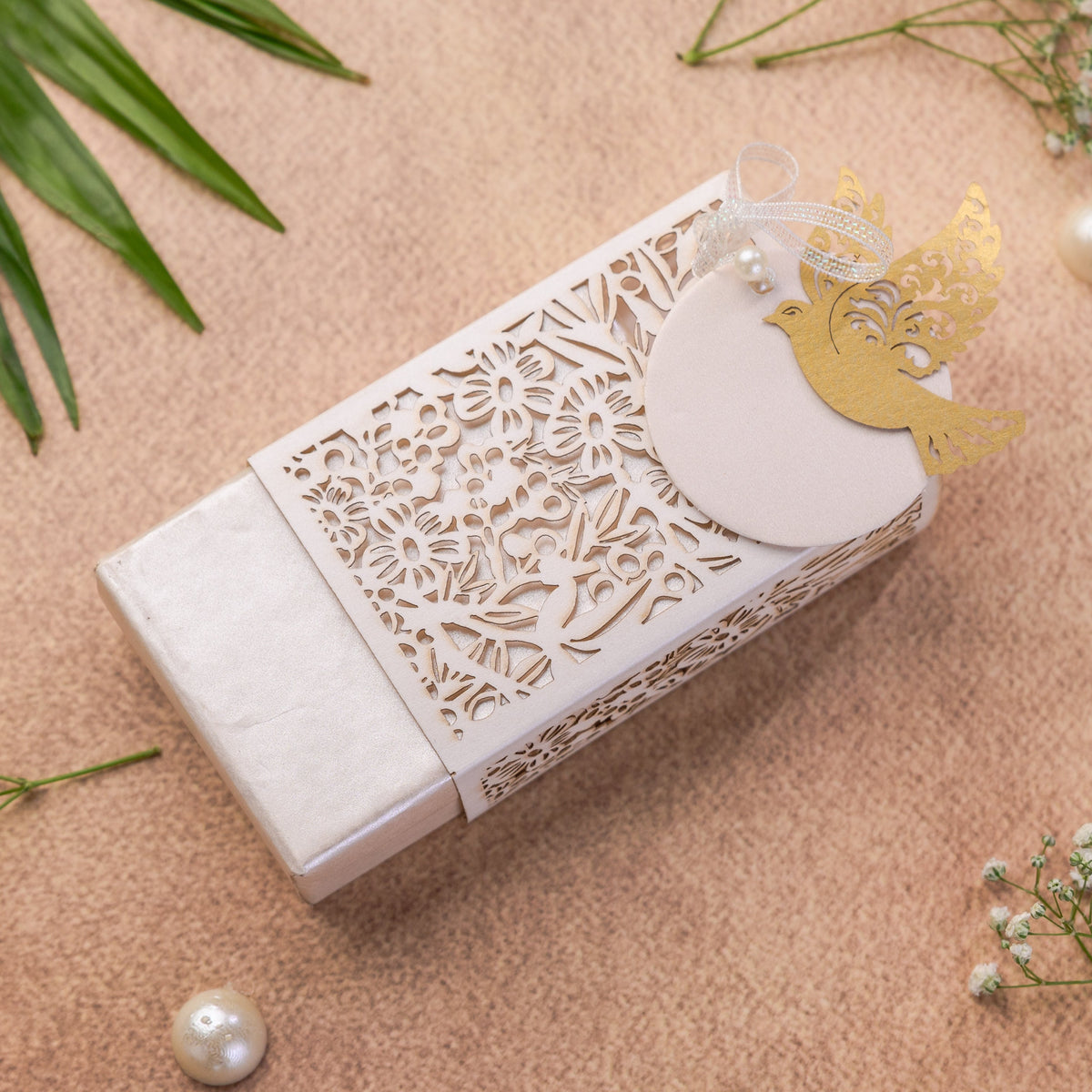 A white rectangular gift box with intricate laser-cut floral patterns on the lid, decorated with a gold bird silhouette and a round white tag