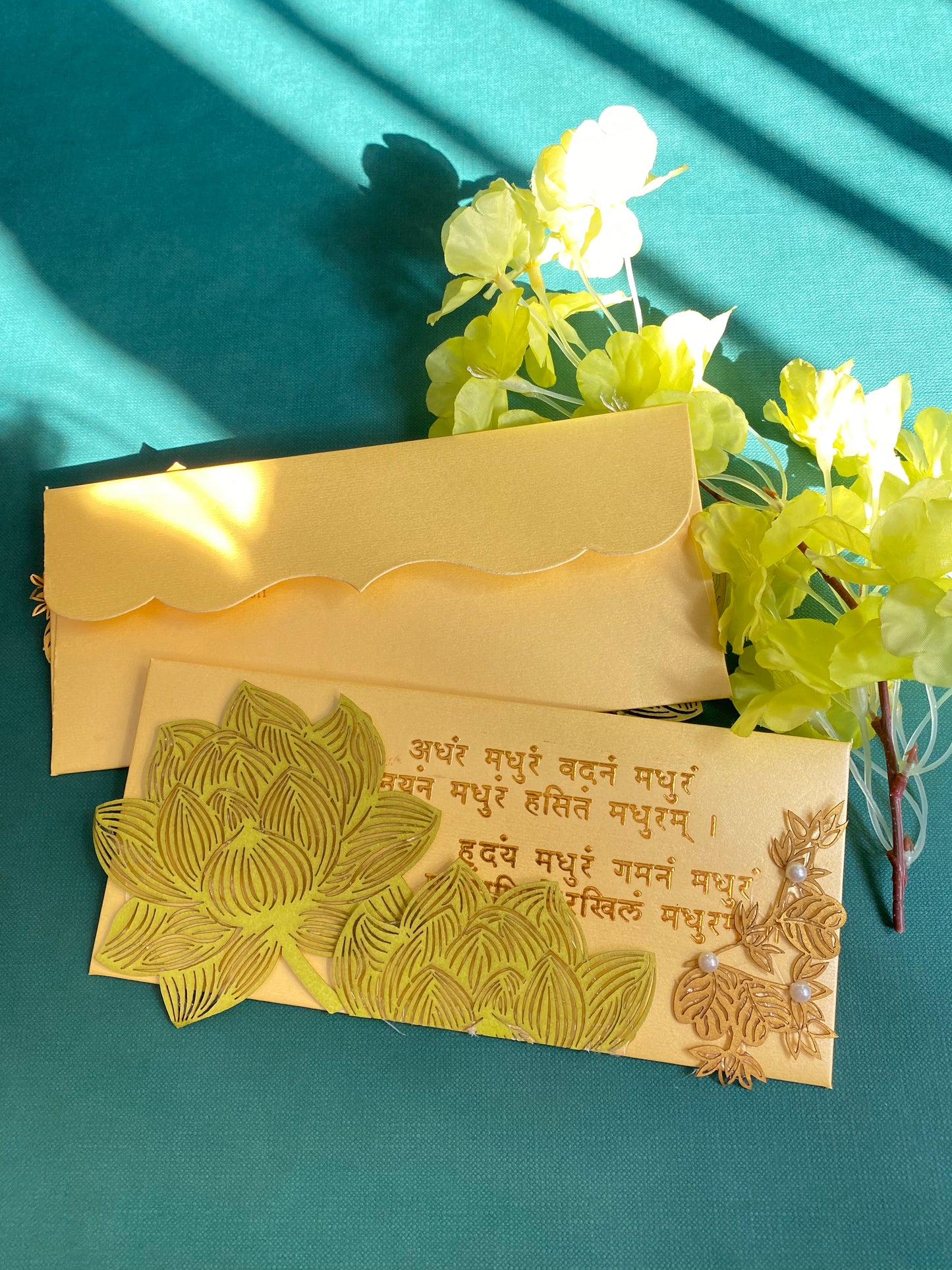 A decorative envelope with laser patchwork in green and gold colors, featuring floral designs and mantra in gold foil. 