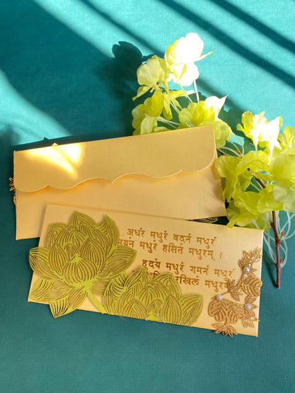 A decorative envelope with laser patchwork in green and gold colors, featuring floral designs and mantra in gold foil. 