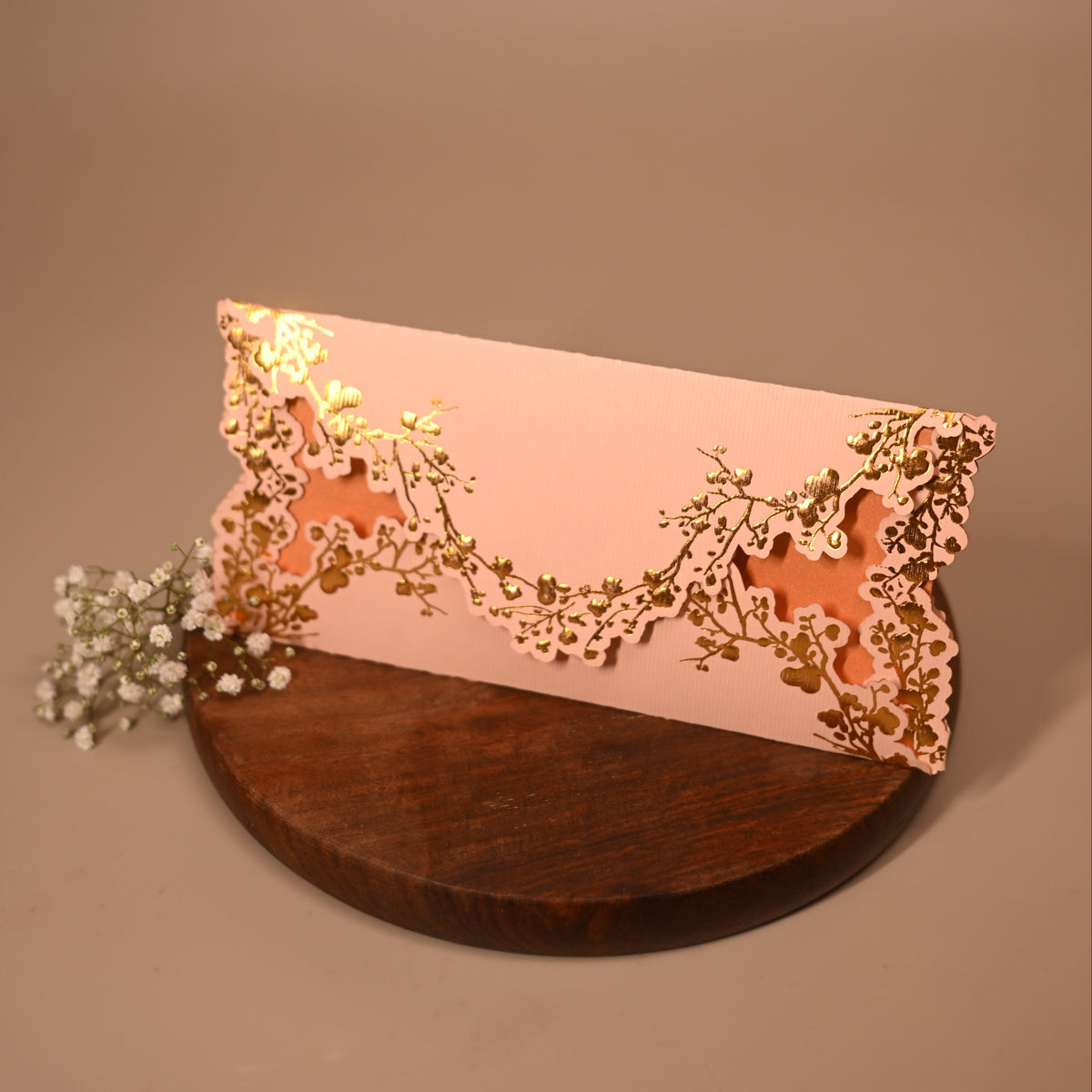 A pale pink envelope with ornate laser-cut floral detailing in gold