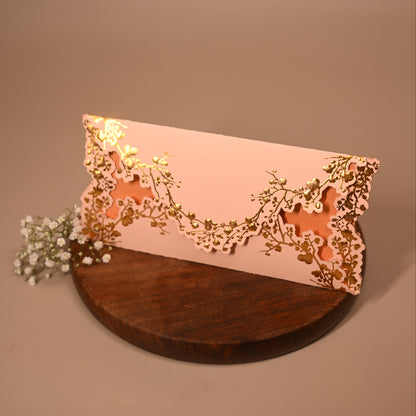A pale pink envelope with ornate laser-cut floral detailing in gold
