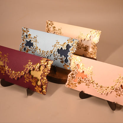 Four rectangular clutch or envelope-style handbags with ornate floral cutout detailing and metallic trim. The visible colors are burgundy, light blue, cream, and blush pink