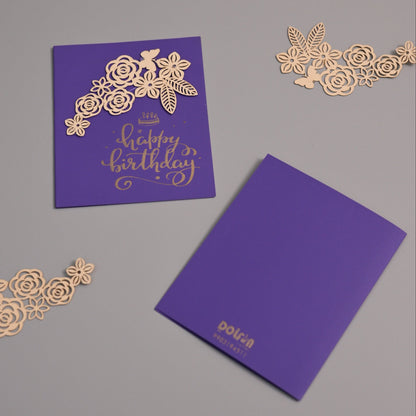 Purple birthday card set with gold foil floral cutout embellishments and a matching purple envelope on a neutral gray background.