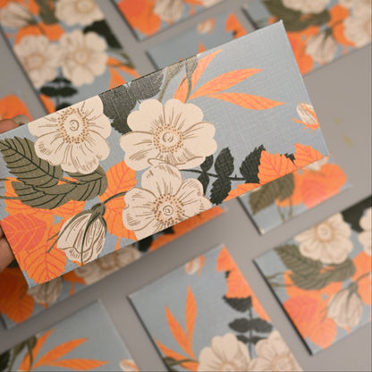 Envelope printed with a floral pattern in orange, cream, olive green, and dark gray on a light blue-gray background.