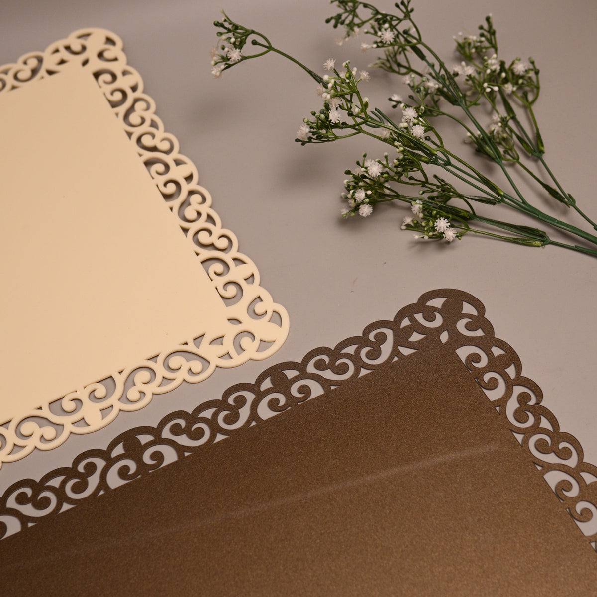 A styled flat-lay of two elegant square paper cards with ornate laser-cut scalloped borders, 