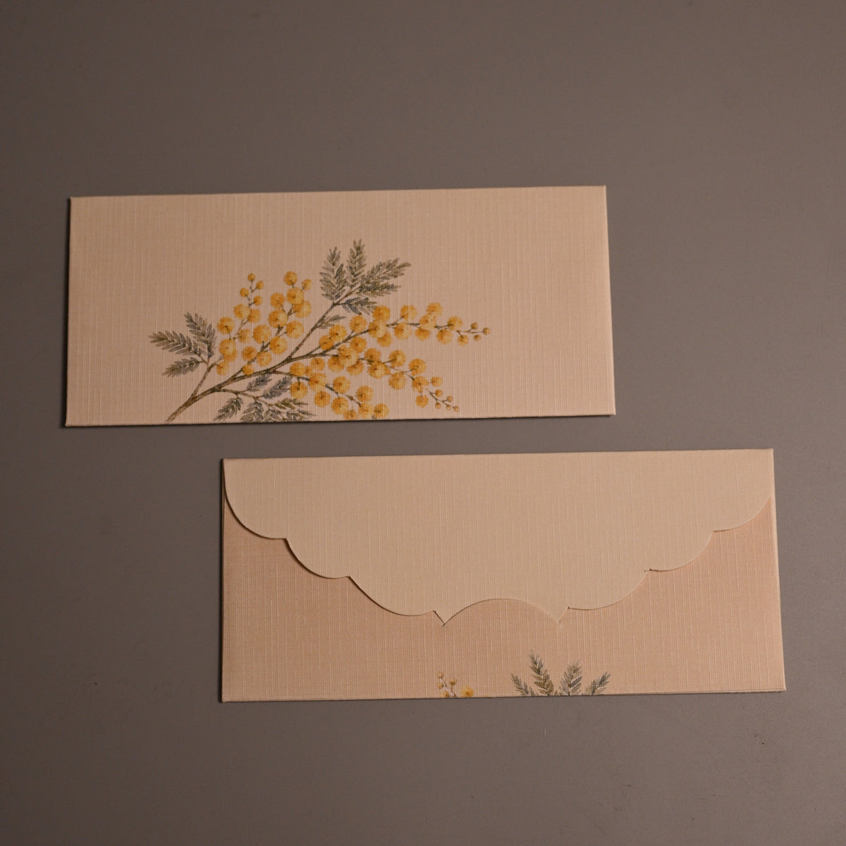 beige envelopes with scalloped edges, one featuring a yellow floral branch 