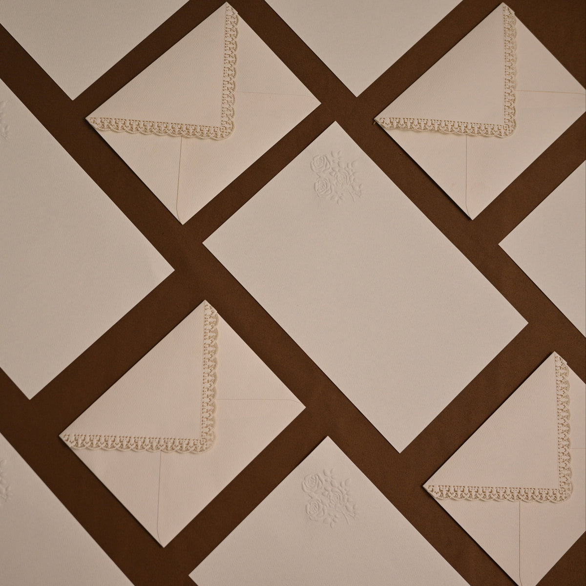 A close-up of a quilted fabric surface with a geometric pattern of cream diamond panels separated by dark brown diagonal bands. Small cream embroidered floral motifs and matching lace trim are visible on some panels.