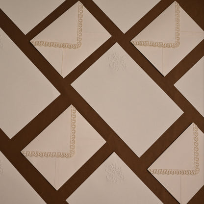 A close-up of a quilted fabric surface with a geometric pattern of cream diamond panels separated by dark brown diagonal bands. Small cream embroidered floral motifs and matching lace trim are visible on some panels.