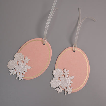 Oval pink gift tags with white rose cutout embellishments and white hanging ribbons.