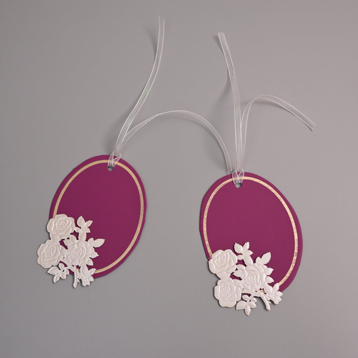 Oval magenta paper gift tags with white floral cutouts and white hanging ribbons.