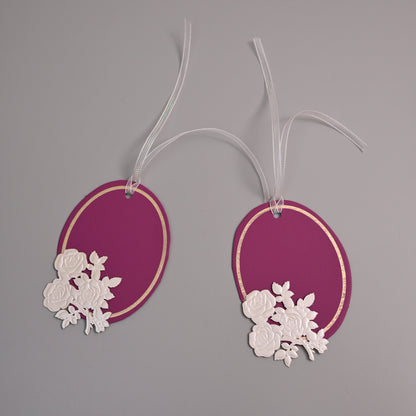 Oval magenta paper gift tags with white floral cutouts and white hanging ribbons.