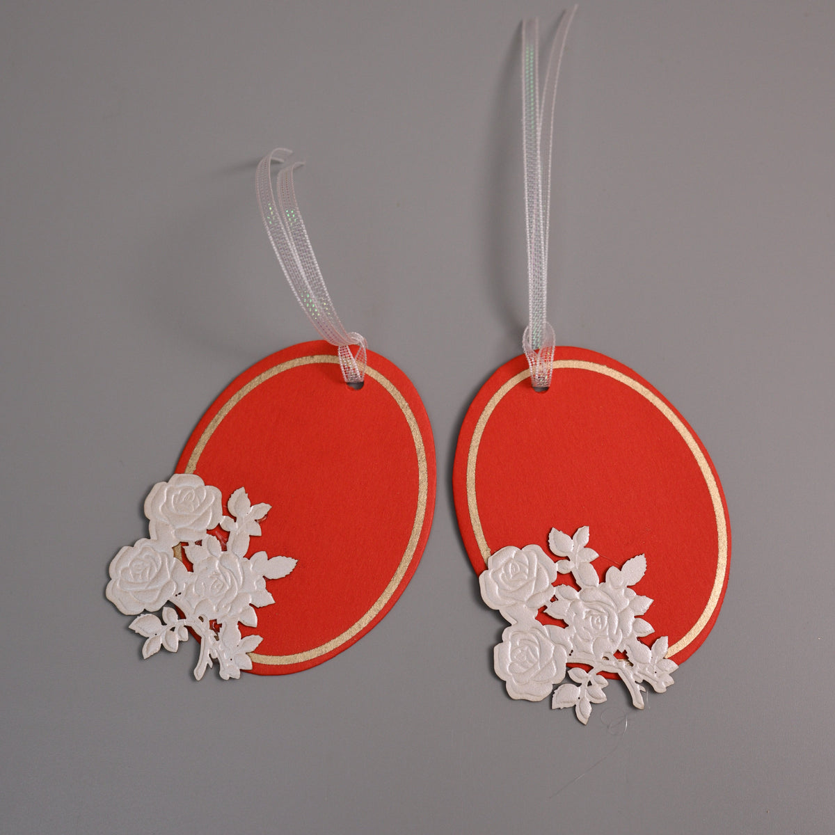 Oval gift tags with white rose cutouts and white hanging ribbons.