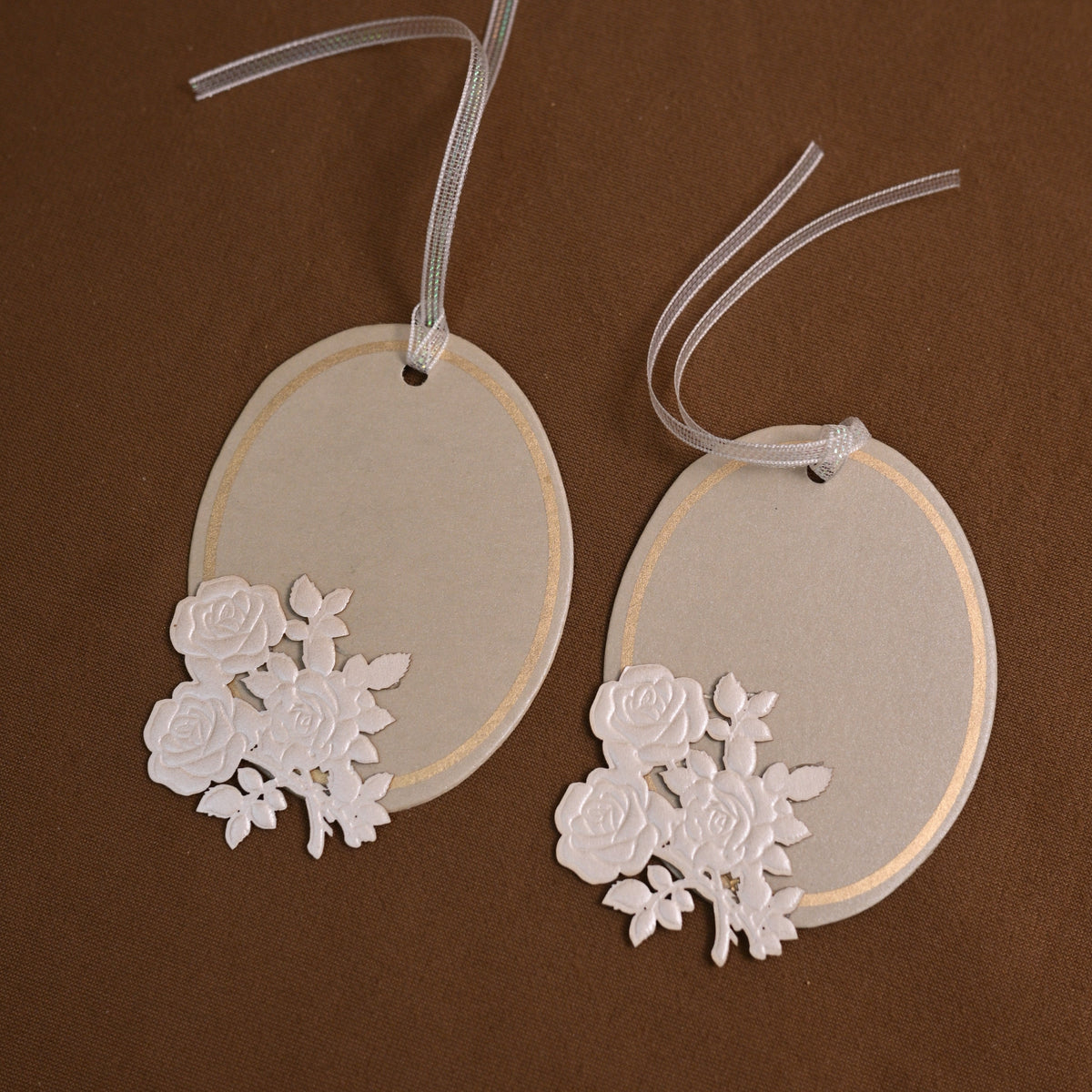 an oval-shaped paper tag or place card featuring an embossed floral applique and a sheer ribbon hanger