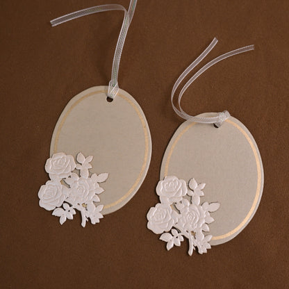 an oval-shaped paper tag or place card featuring an embossed floral applique and a sheer ribbon hanger