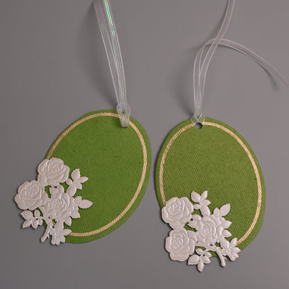 Two green oval gift tags with white floral cutout embellishments and white ribbons