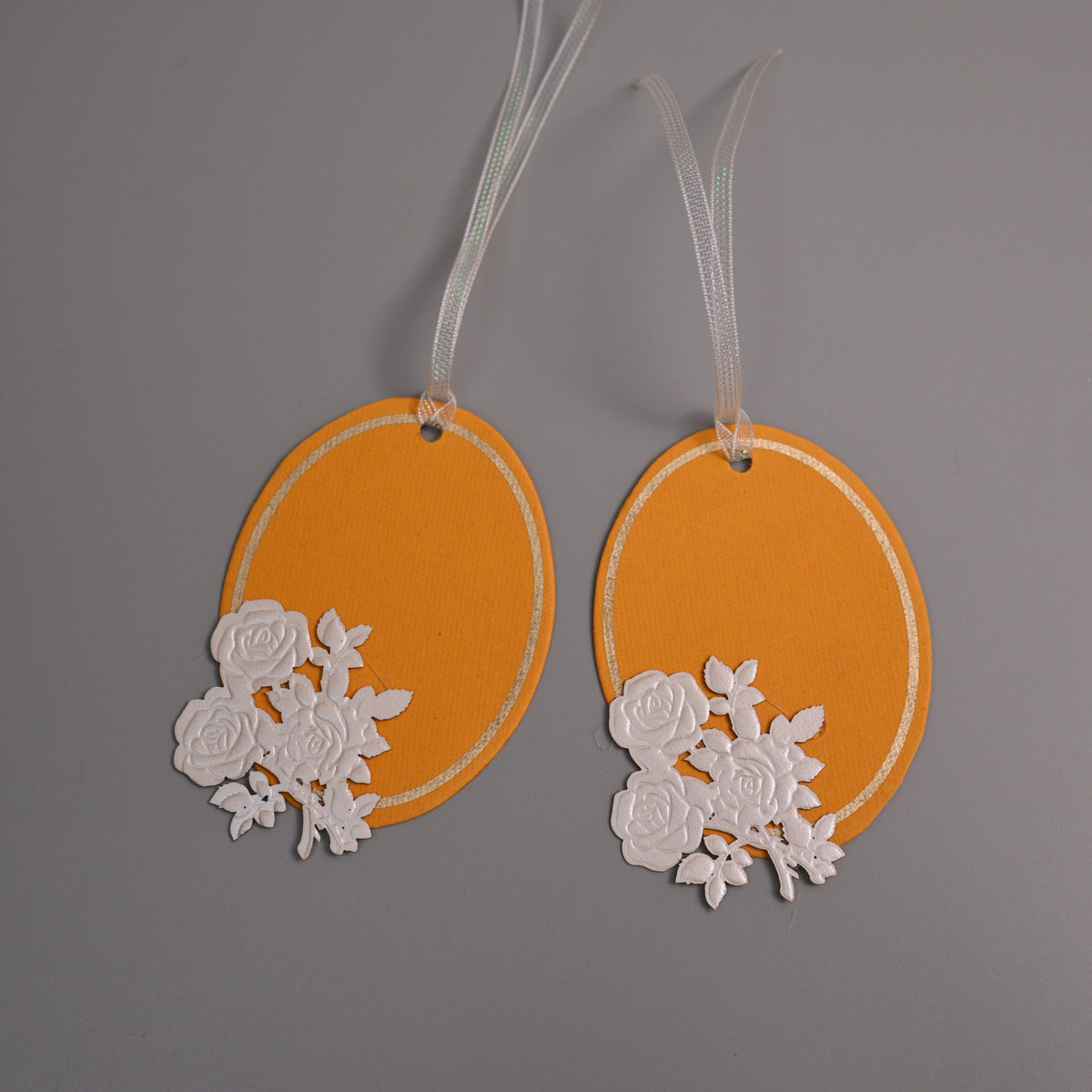 Oval gift tags in orange with white rose cutouts and white ribbons.