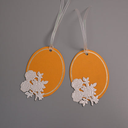 Oval gift tags in orange with white rose cutouts and white ribbons.