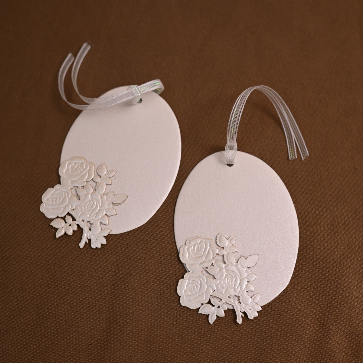 Two oval magenta gift tags with white floral cutouts and white ribbons, displayed on a neutral gray background.