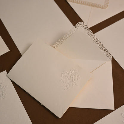 White embossed stationery cards and envelopes with delicate lace trim, arranged on a dark brown geometric background.